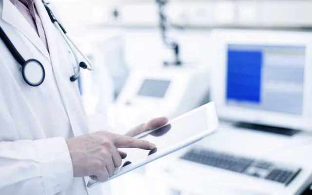 Clinician reviewing patient information on a tablet beside clinical monitors